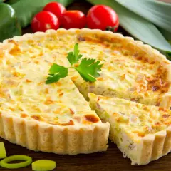 Quiche Lorraine con pasta sfoglia, un classico della cucina francese, con una fetta tagliata per mostrare il ripieno cremoso e saporito.
