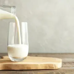 Mleko przelewane z butelki do szklanki na drewnianej desce.