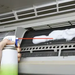 Mano rociando espuma limpiadora en las aletas de un aire acondicionado para limpiar bandeja aire acondicionado.