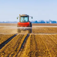 Czerwony traktor rozsiewa wapno z magnezem na polu, przygotowując ziemię do nowego sezonu.