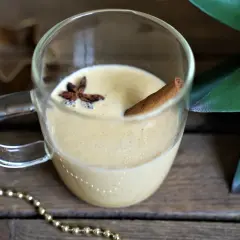 Un verre de lait de poule crémeux, garni d'anis étoilé et d'un bâton de cannelle, sur fond de bois rustique.