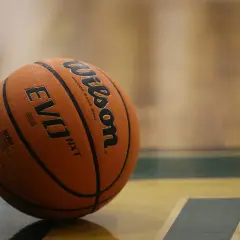 Pomarańczowa piłka Wilson Evo NXT leży na parkiecie hali sportowej, gotowa do gry.