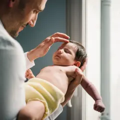 Sanfte Hände eines Mannes führen eine sanfte osteopathische Behandlung bei einem schlafenden Neugeborenen durch.