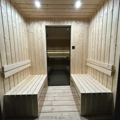 Drewniana sauna z ławami i szklanymi drzwiami. Dyskretna wentylacja w saunie zapewnia komfort.