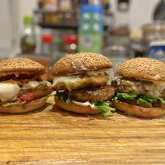 Trois burgers gras appétissants, garnis de fromage fondant, légumes frais et tomates séchées, prêts à être dégustés.