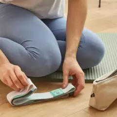 Kobieta w legginsach przygotowuje pasek do jogi na macie. Obok leży woreczek.