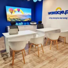 Nowoczesne biuro z logo "wakacje.pl", ekranem z balonami i białymi biurkami.