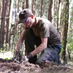 Mężczyzna w lesie przygotowuje rozpałkę. To pokazuje, survival co to znaczy: umiejętność radzenia sobie w trudnych warunkach.
