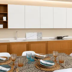 Elegantes cocinas modernas blancas con gabinetes de madera, encimera de cuarzo y mesa lista para cenar.
