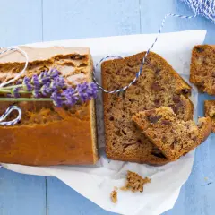 Pokrojony chlebek bananowy z gałązką lawendy i sznurkiem na niebieskim tle.