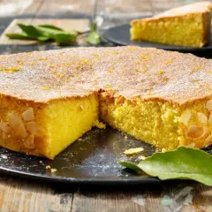 Deliziosa caprese al limone, con mandorle tostate sui bordi e scorza d'arancia in superficie, spolverata di zucchero a velo.
