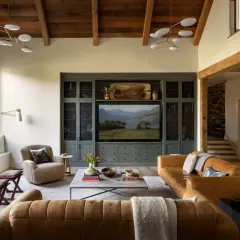 Cozy living room in a ranch style house featuring leather sofas, a stone fireplace, and a built-in entertainment center with a landscape painting.