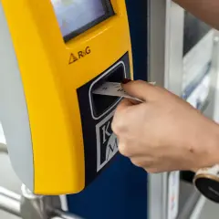 Ręka z zegarkiem wkłada bilet godzinny Kraków do żółtego automatu.