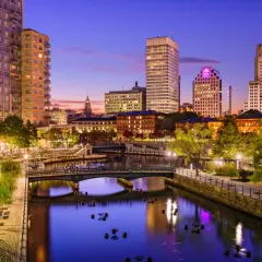 Wieczorny widok na Providence, stolicę najmniejszego stanu USA, Rhode Island. Rzeka otoczona budynkami i zielenią.