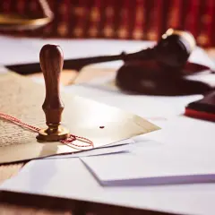 Pieczęć lakowa na dokumencie, młotek sędziowski i waga szalkowa. Symbolizują prawo i porządek, a także to, kto to prokurent – osoba upoważniona do reprezentowania firmy.