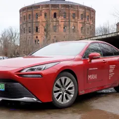 Czerwona Toyota Mirai z napisem "Zasięg na jednym tankowaniu do 650 km" stoi przed zabytkową gazownią.