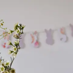 Delikatne kwiaty na pierwszym planie, w tle pastelowa girlanda do druku z króliczkami.