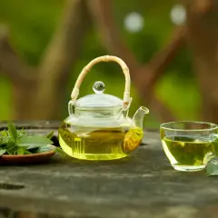 Tetera de cristal con té verde y hojas frescas. Descubre para qué sirve el té verde y sus beneficios.