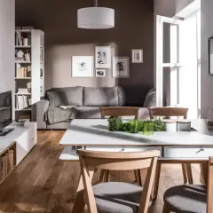 Nowoczesny, prostokątny salon z jadalnią. Szara kanapa, białe meble, drewniana podłoga i jasne dodatki tworzą przytulną atmosferę.