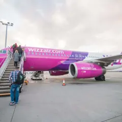 Pasażerowie wsiadają po schodkach do różowo-fioletowego samolotu Wizz Air.