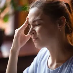 Kobieta z bólem głowy, być może objaw POTS. Dłoń na skroni, zmarszczone czoło.