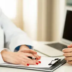 Lekarz w białym fartuchu z notatnikiem i długopisem rozmawia z pacjentem.