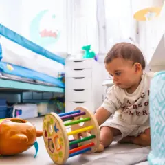 Małe dziecko bawi się zabawkami na podłodze. Idealny stosunek **ile dzieci na jednego opiekuna** pozwala na taką swobodę.