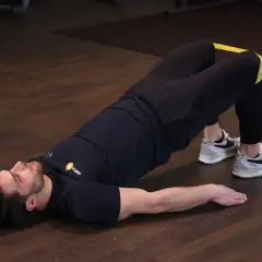Mężczyzna wykonuje ćwiczenie glute bridge z gumą na udach, napinając pośladki.