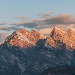 Goldene Abendsonne beleuchtet die schroffen Gipfel der Drei Zinnen. Das Wetter ist klar, mit zarten Wolken am Himmel.