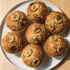 Sju gyllene bananmuffins med skivor av banan på toppen, redo att avnjutas. Ett perfekt bananmuffins recept!