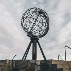 Metalowy glob na statywie na tle pochmurnego nieba, widok z dołu.