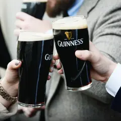 Dwie osoby wznoszą toast szklankami ciemnego piwa Guinness. To klasyczne piwo ma ok. 4,2% alkoholu.