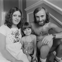 Phil Collins z żoną i córką, uśmiechnięci, siedzą na schodach.