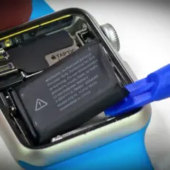 Wymiana baterii Apple Watch: wyjmowanie starego ogniwa za pomocą niebieskiego narzędzia.