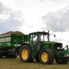 Zielony traktor John Deere z przyczepą pełną ziemniaków, wyposażoną w hamulec najazdowy, gotowy do pracy na polu.