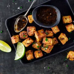 Tofu in padella dorato e croccante, servito con salsa e spicchi di lime.