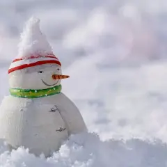 Mały bałwanek w czapce i szaliku, otoczony śniegiem. Czeka, aż spadnie więcej śniegu, by mógł się bawić.