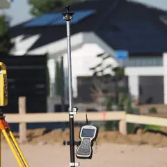 Żółty tachimetr geodezyjny i tyczka z odbiornikiem GPS na budowie.