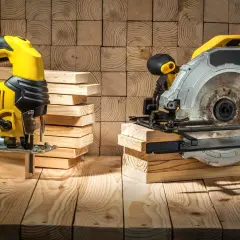 Scie sauteuse jaune et scie circulaire argentée, prêtes à découper du bois. La différence entre ces outils est claire pour tout bricoleur.