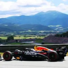 Un coche de Red Bull compite en el Gran Premio de Austria, con montañas y público al fondo.