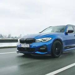 Niebieskie BMW 330e na mokrej drodze, z widocznymi kroplami deszczu na karoserii.