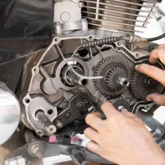 Mani che lavorano sul motore di una moto, ingranaggi visibili. Possibili cause di perdita potenza motore diesel.