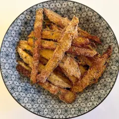 Bastoncini di melanzane impanate, un classico delle ricette della nonna, serviti in una ciotola decorata.