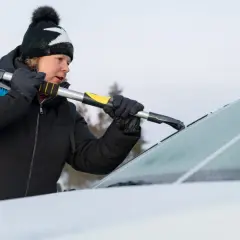 Kvinna skrapar is från bilruta med isskrapa. Kallstart bil kräver förberedelse.