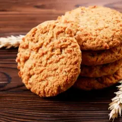 Biscotti integrali da colazione dorati e croccanti, impilati su un tavolo di legno scuro, con spighe di grano a lato.
