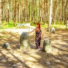 Kobieta z rudymi włosami stoi między kamieniami w lesie.