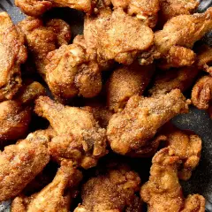 A pile of crispy, golden-brown Nagoya style chicken wings, seasoned with spices, on a dark plate.