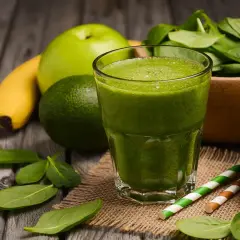 Zielony koktajl owocowy z bananem, jabłkiem i awokado, otoczony świeżymi liśćmi szpinaku.