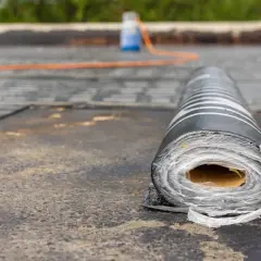 Rolka papy na dachu, gotowa do pracy. W tle pomarańczowy wąż i butla z płynem, wskazujące na proces, jak kłaść papę.