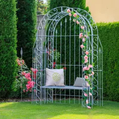Ein weißer Rosenbogen mit rosa Rosen, Sitzbank und Kissen. Tolle Rosenbogen Gestaltungsideen für Ihren Garten.